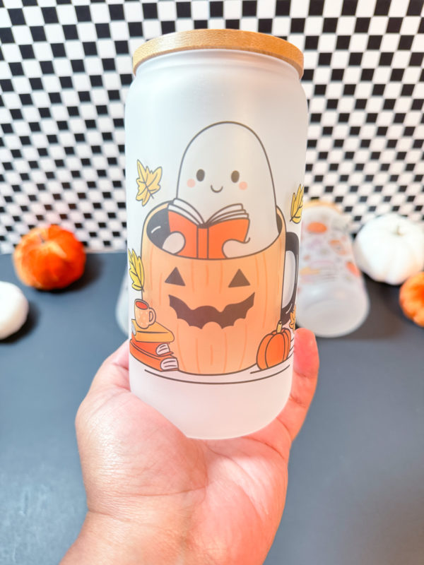 Cute Ghost sitting inside a pumpkin reading a book surrounds by books, leaves, coffee cup, and pumpkins