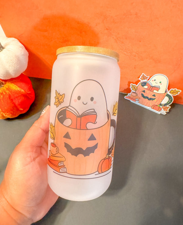 Cute Ghost sitting inside a pumpkin reading a book surrounds by books, leaves, coffee cup, and pumpkins