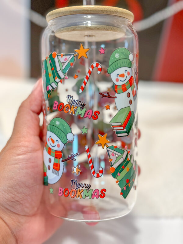 This Merry Bookmas 16oz glass can is the ultimate bookish gift for the holiday season! Designed for book lovers and Christmas enthusiasts alike, this double-sided UV DTF tumbler features a whimsical Christmas tree made of books, a cheerful snowman, candy canes, stars, and festive lights—all in a bright, colorful design that celebrates the coziness of the season.